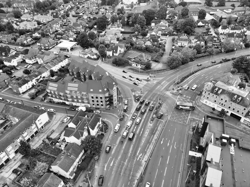 An aerial black-and-white photograph of a busy residential area in Kidbrooke, showing a main road with multiple lanes of traffic, including cars, taxis, and vans, moving in both directions. A large va