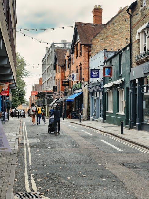 A narrow residential street in Kidbrooke with a gently curved road made of asphalt, lined with two to three-storey terraced houses on both sides. The houses are painted in pastel shades of light blue,