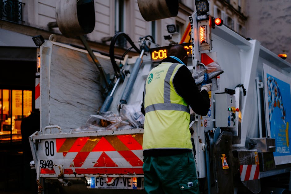 A white sedan with significant front-end damage, including a crumpled hood and broken bumper, is positioned on top of a flatbed tow truck, ready for removal. The vehicle is inside an industrial wareho